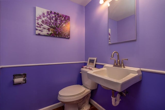 half bathroom featuring a sink, baseboards, and toilet