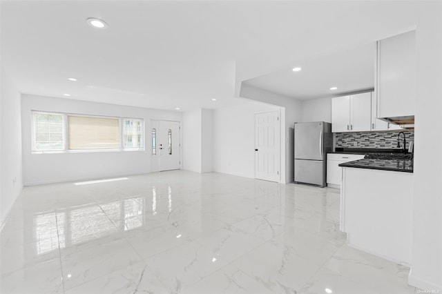 kitchen with dark countertops, freestanding refrigerator, marble finish floor, white cabinetry, and backsplash