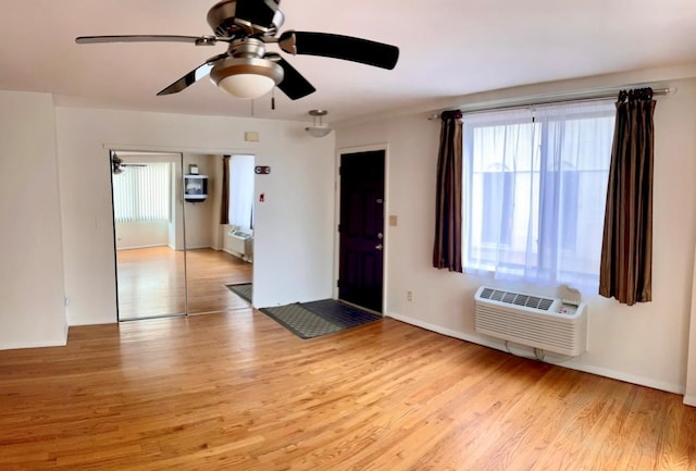 foyer entrance with a wall unit AC, light wood finished floors, and a ceiling fan