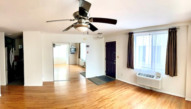 spare room featuring light wood-style floors, a ceiling fan, and a wall mounted AC