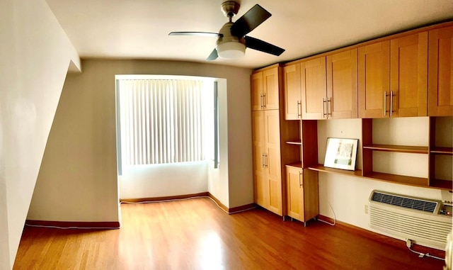 interior space featuring a ceiling fan, a wall mounted AC, baseboards, and wood finished floors