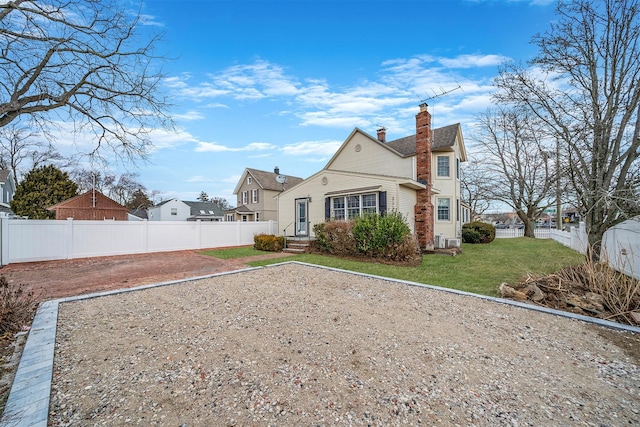 rear view of house featuring a fenced backyard, a yard, and a chimney