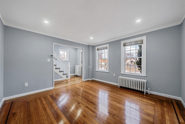 empty room featuring baseboards, hardwood / wood-style flooring, radiator heating unit, stairway, and ornamental molding