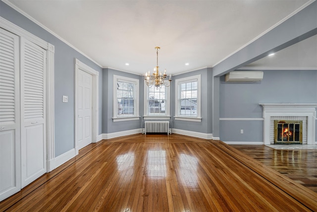 unfurnished dining area featuring radiator heating unit, a wall mounted AC, a brick fireplace, baseboards, and hardwood / wood-style flooring