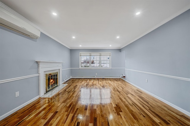 unfurnished living room featuring a wall unit AC, a brick fireplace, ornamental molding, and hardwood / wood-style flooring