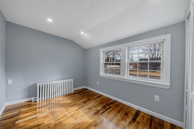 empty room with radiator, vaulted ceiling, baseboards, and wood finished floors