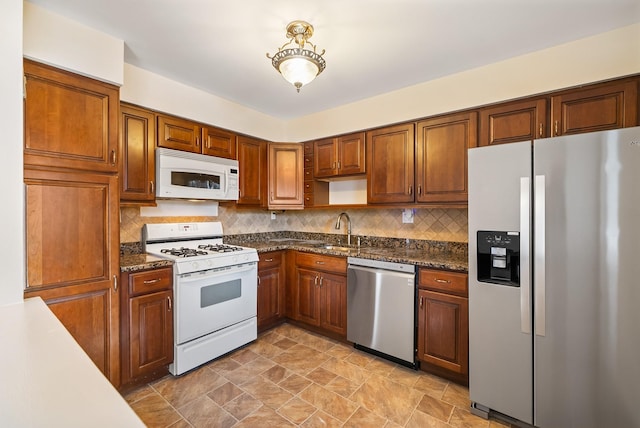 kitchen with appliances with stainless steel finishes, brown cabinetry, a sink, and backsplash