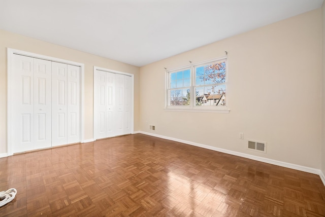 unfurnished bedroom featuring baseboards, visible vents, and two closets