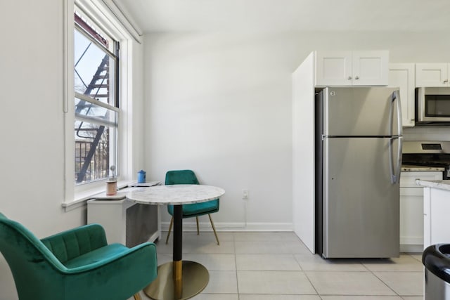 kitchen with light tile patterned floors, appliances with stainless steel finishes, white cabinetry, and baseboards