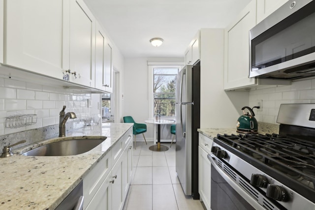 kitchen with light tile patterned floors, stainless steel appliances, a sink, white cabinetry, and tasteful backsplash