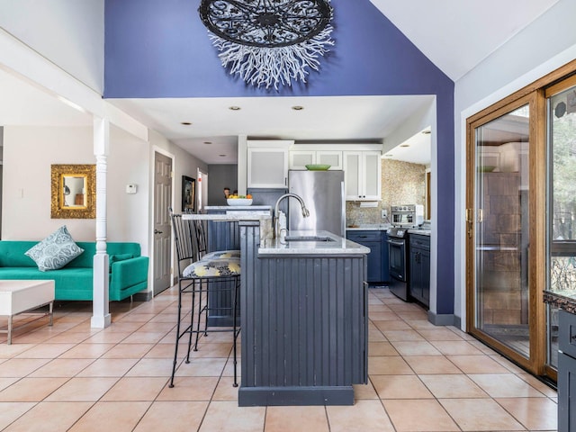 kitchen with light tile patterned floors, decorative backsplash, appliances with stainless steel finishes, white cabinetry, and a kitchen breakfast bar