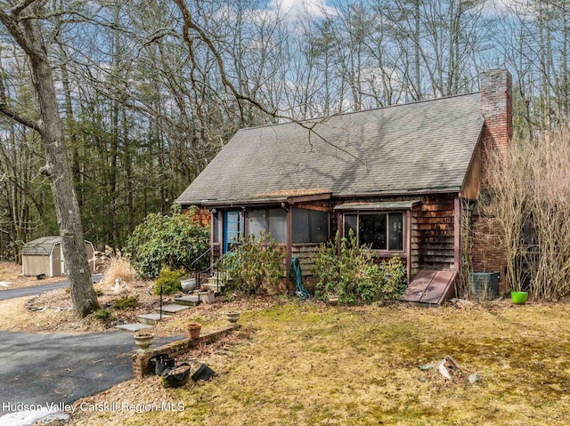 rustic home featuring an outbuilding, a shed, a chimney, and roof with shingles