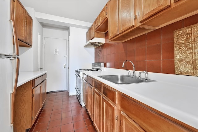 kitchen featuring dark tile patterned floors, a sink, freestanding refrigerator, decorative backsplash, and stainless steel range with gas stovetop