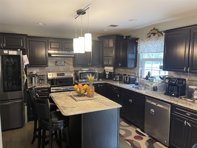 kitchen featuring tasteful backsplash, visible vents, a kitchen island, appliances with stainless steel finishes, and under cabinet range hood