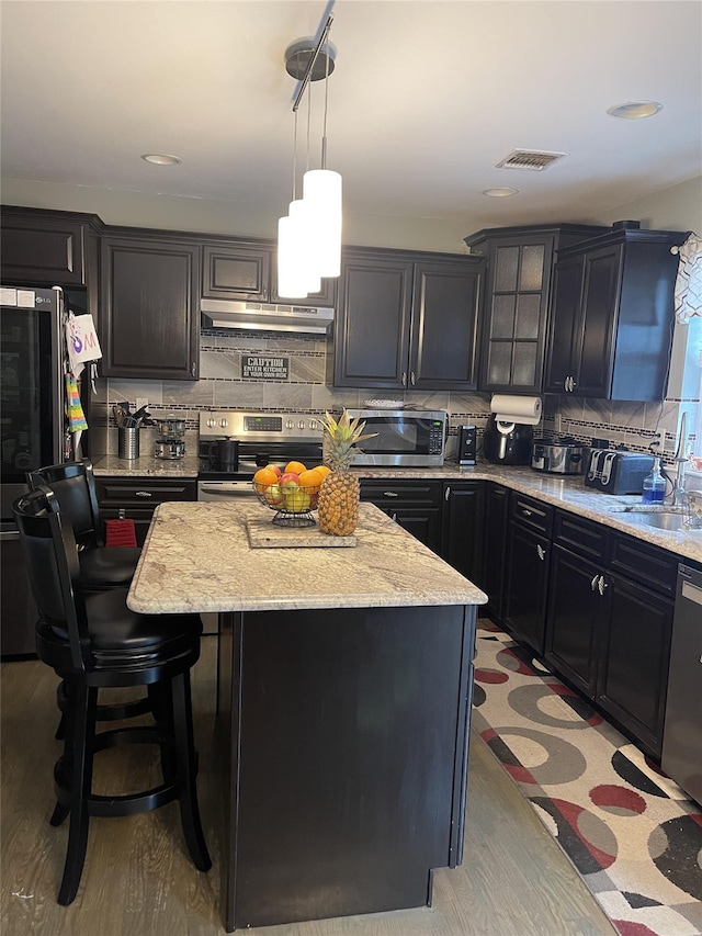 kitchen with visible vents, decorative backsplash, appliances with stainless steel finishes, a kitchen island, and under cabinet range hood