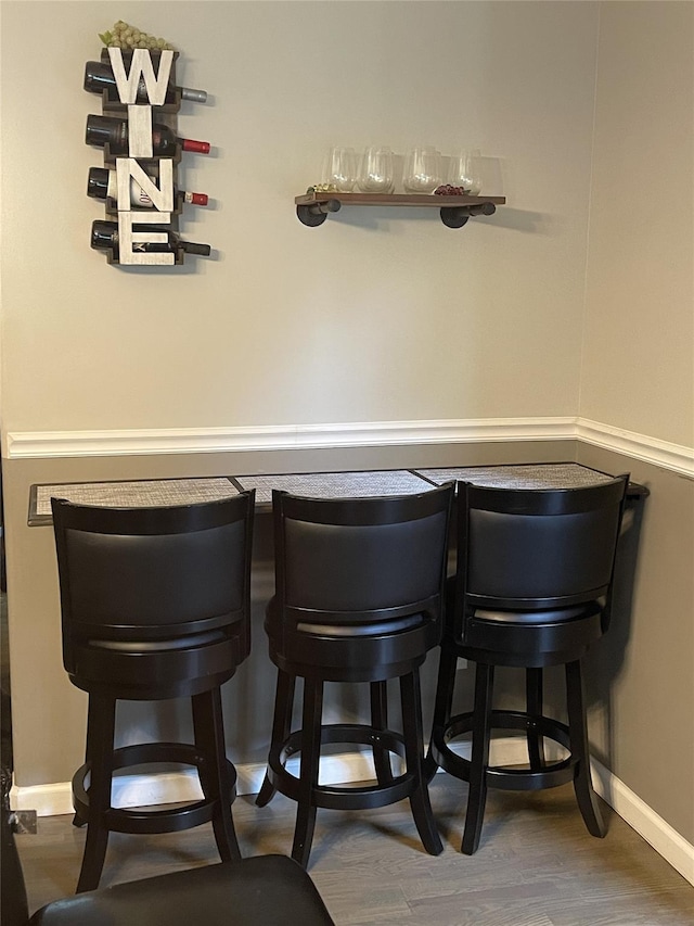 bar featuring a bar, wood finished floors, and baseboards