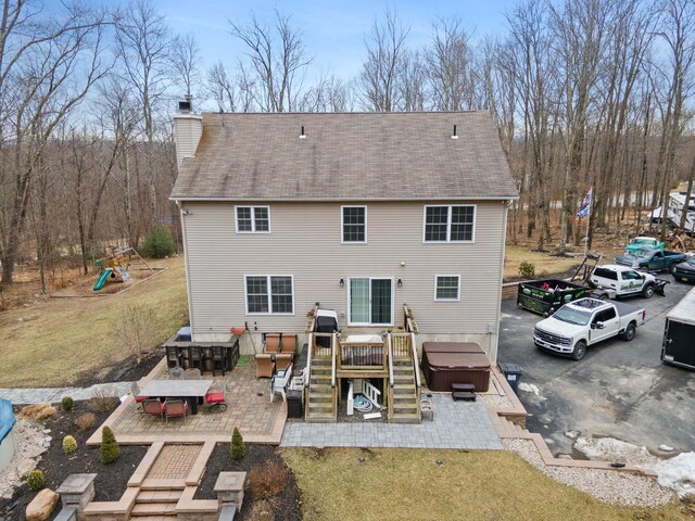 rear view of property featuring a patio, a playground, a wooden deck, a chimney, and a hot tub