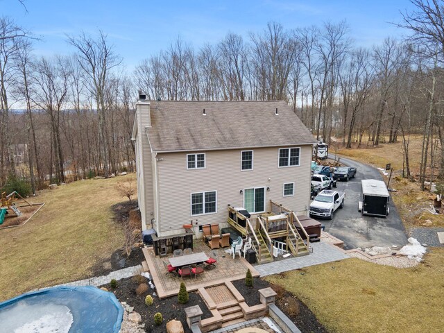 rear view of property with a deck, a yard, roof with shingles, outdoor dining area, and a chimney