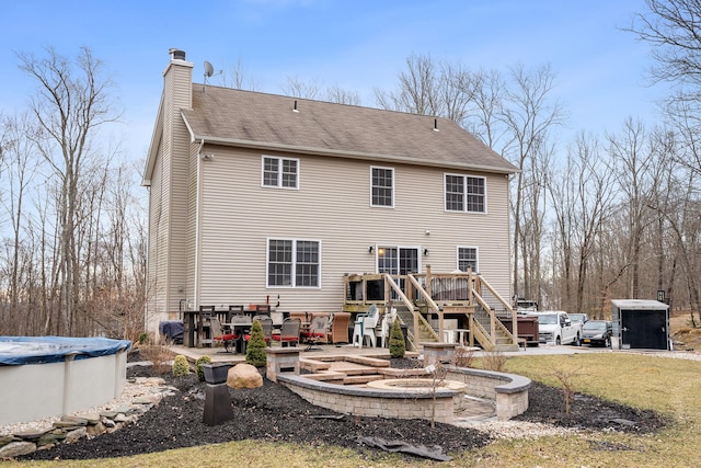 rear view of property with a deck, a covered pool, roof with shingles, a chimney, and a patio area