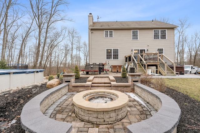 back of property featuring a deck, a covered pool, a fire pit, a chimney, and a patio area