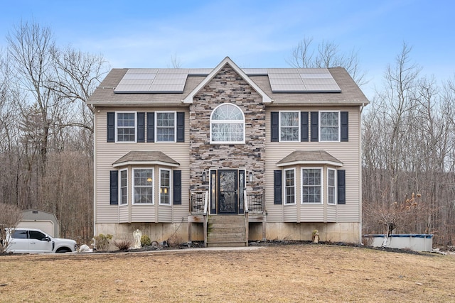 view of front facade featuring roof mounted solar panels, a front yard, and roof with shingles