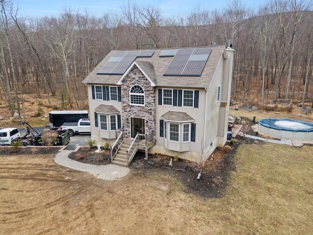 view of front of house with a view of trees, solar panels, and a chimney