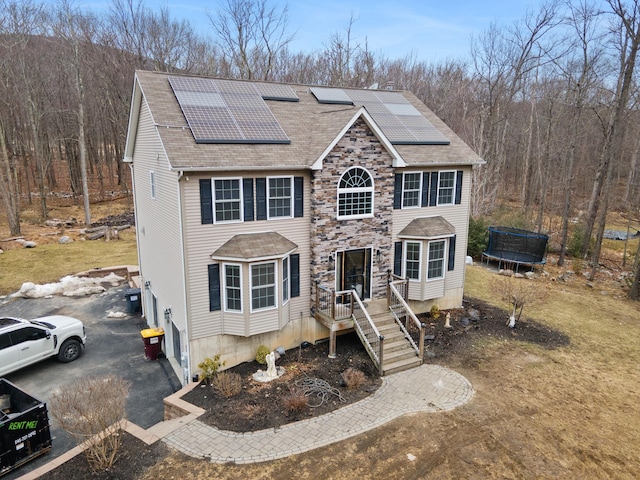 view of front of home with roof mounted solar panels, a trampoline, and roof with shingles