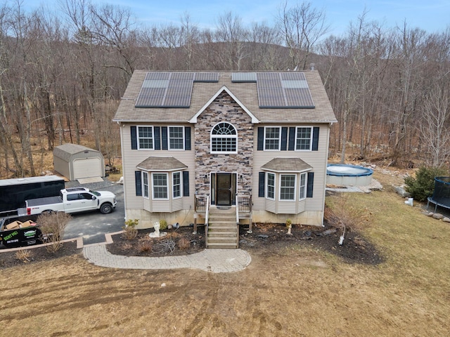 view of front of property with solar panels, an outdoor structure, a trampoline, and stone siding