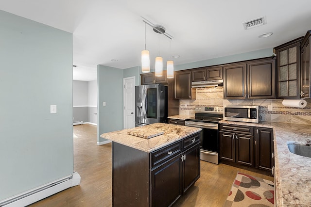 kitchen featuring visible vents, under cabinet range hood, appliances with stainless steel finishes, a baseboard heating unit, and tasteful backsplash