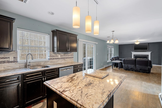 kitchen featuring light stone countertops, a sink, stainless steel dishwasher, tasteful backsplash, and open floor plan