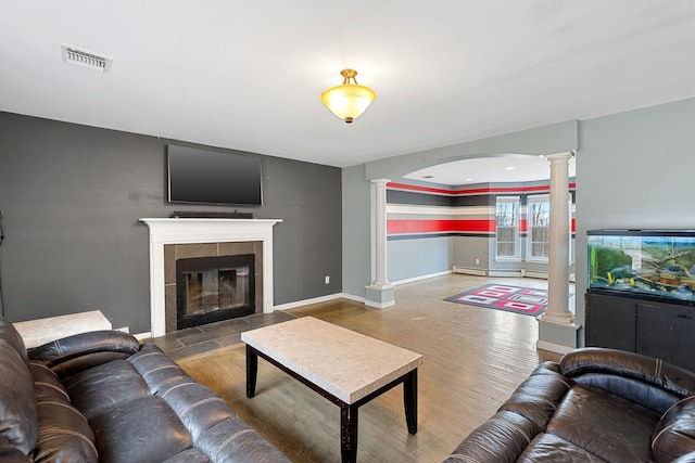 living area featuring visible vents, decorative columns, a tile fireplace, wood finished floors, and a baseboard radiator