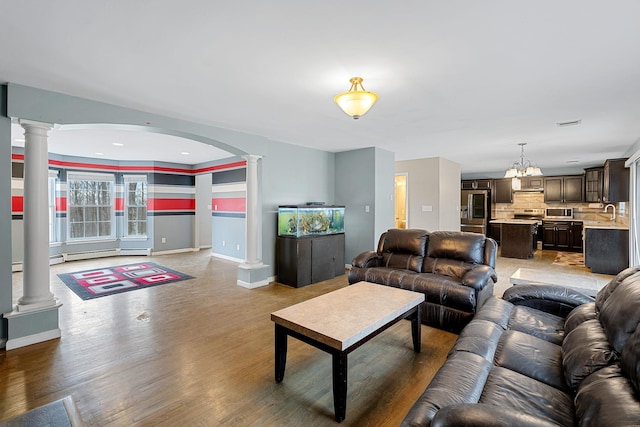 living area with arched walkways, baseboards, light wood-style floors, and ornate columns