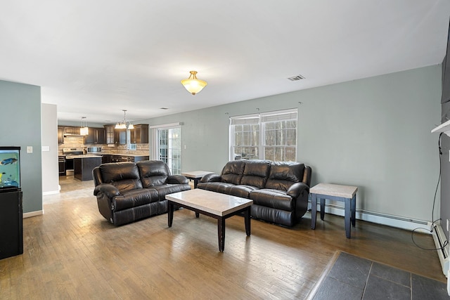 living room with visible vents, baseboards, a chandelier, hardwood / wood-style floors, and baseboard heating