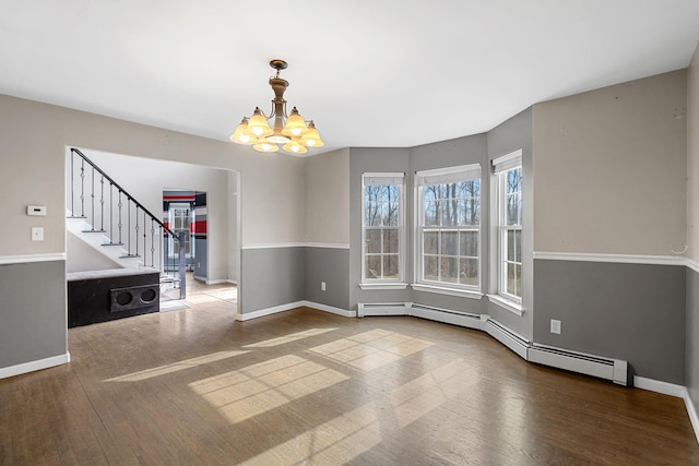 spare room featuring baseboards, stairs, hardwood / wood-style flooring, a baseboard heating unit, and a notable chandelier
