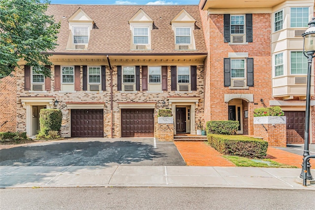 townhome / multi-family property with driveway, a shingled roof, an attached garage, cooling unit, and brick siding