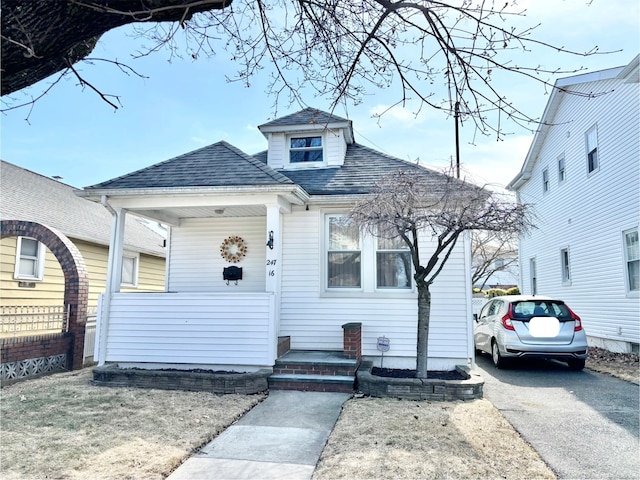 bungalow-style home with driveway, covered porch, and roof with shingles