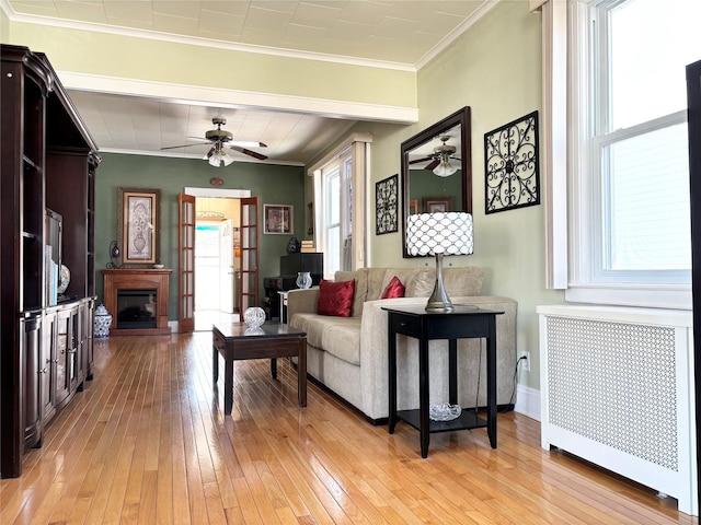 living area with radiator, a fireplace, crown molding, and light wood-style flooring