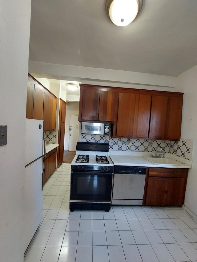 kitchen featuring light tile patterned floors, stainless steel appliances, a sink, light countertops, and tasteful backsplash