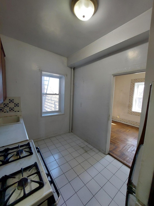 kitchen featuring white range with gas cooktop, light countertops, a sink, and light tile patterned flooring