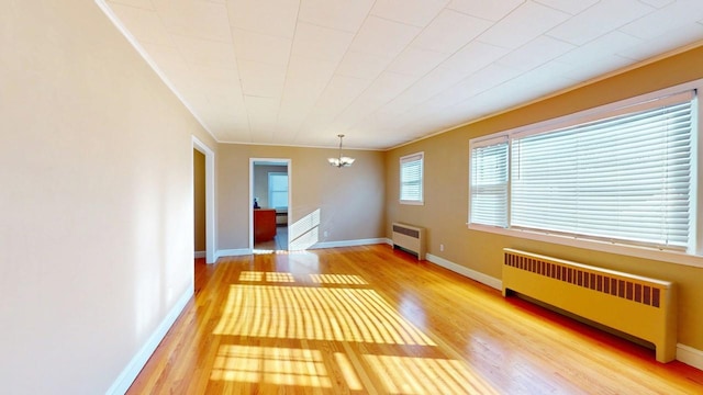 empty room featuring a chandelier, baseboards, wood finished floors, and radiator