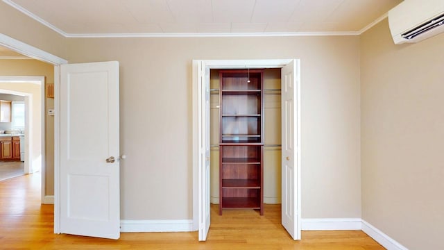 interior space with baseboards, an AC wall unit, crown molding, and light wood-style floors