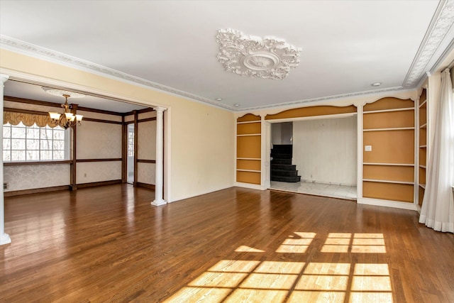 unfurnished living room with ornamental molding, a notable chandelier, stairway, and wood finished floors