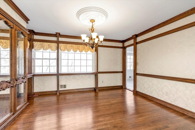 unfurnished room with wood finished floors, visible vents, ornamental molding, wallpapered walls, and an inviting chandelier