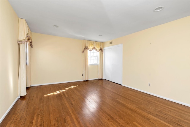 spare room with wood finished floors, visible vents, and baseboards