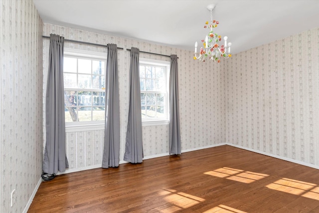 unfurnished room featuring a chandelier, baseboards, wood finished floors, and wallpapered walls