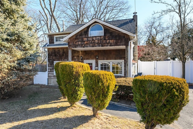 view of front of house featuring a shingled roof, fence, and a chimney