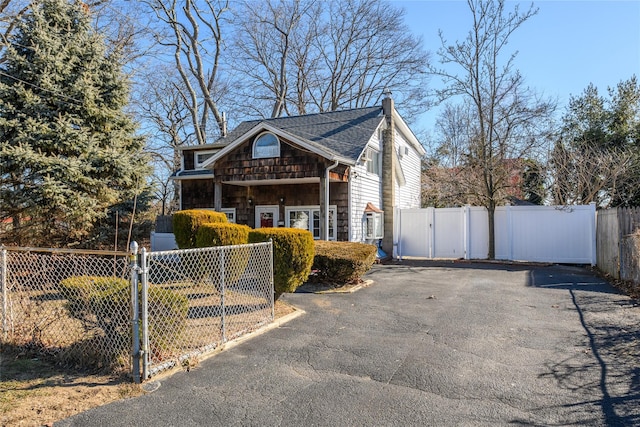 view of front of house with a fenced front yard, aphalt driveway, a chimney, a shingled roof, and a gate