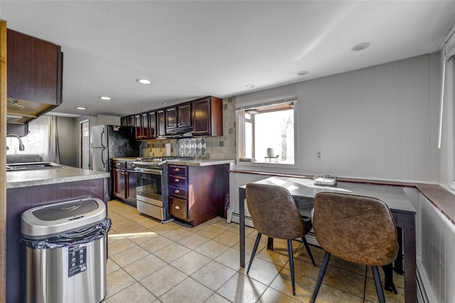 kitchen with light tile patterned floors, decorative backsplash, stainless steel range with gas stovetop, light countertops, and a sink