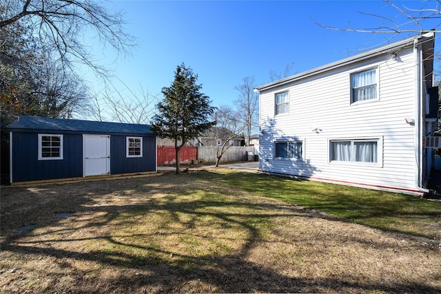 back of property featuring fence, a lawn, and an outbuilding