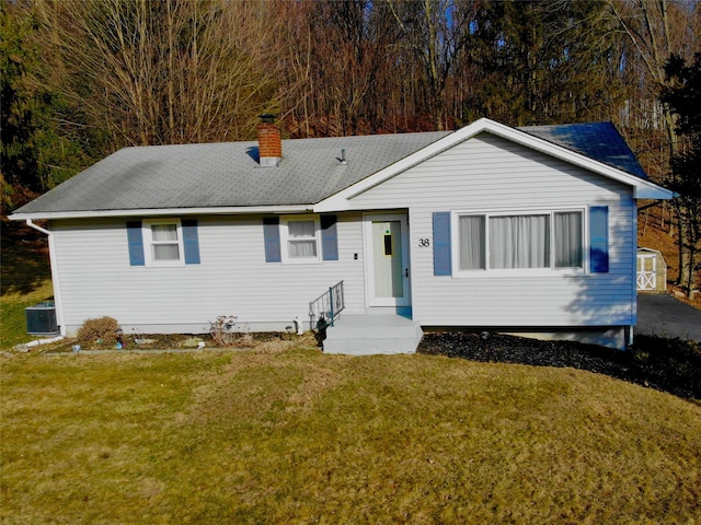 view of front facade featuring central AC unit, a chimney, a front lawn, and a shingled roof